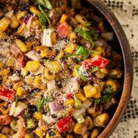 A wooden bowl of Mexican corn salad on a table with a lace table cloth.