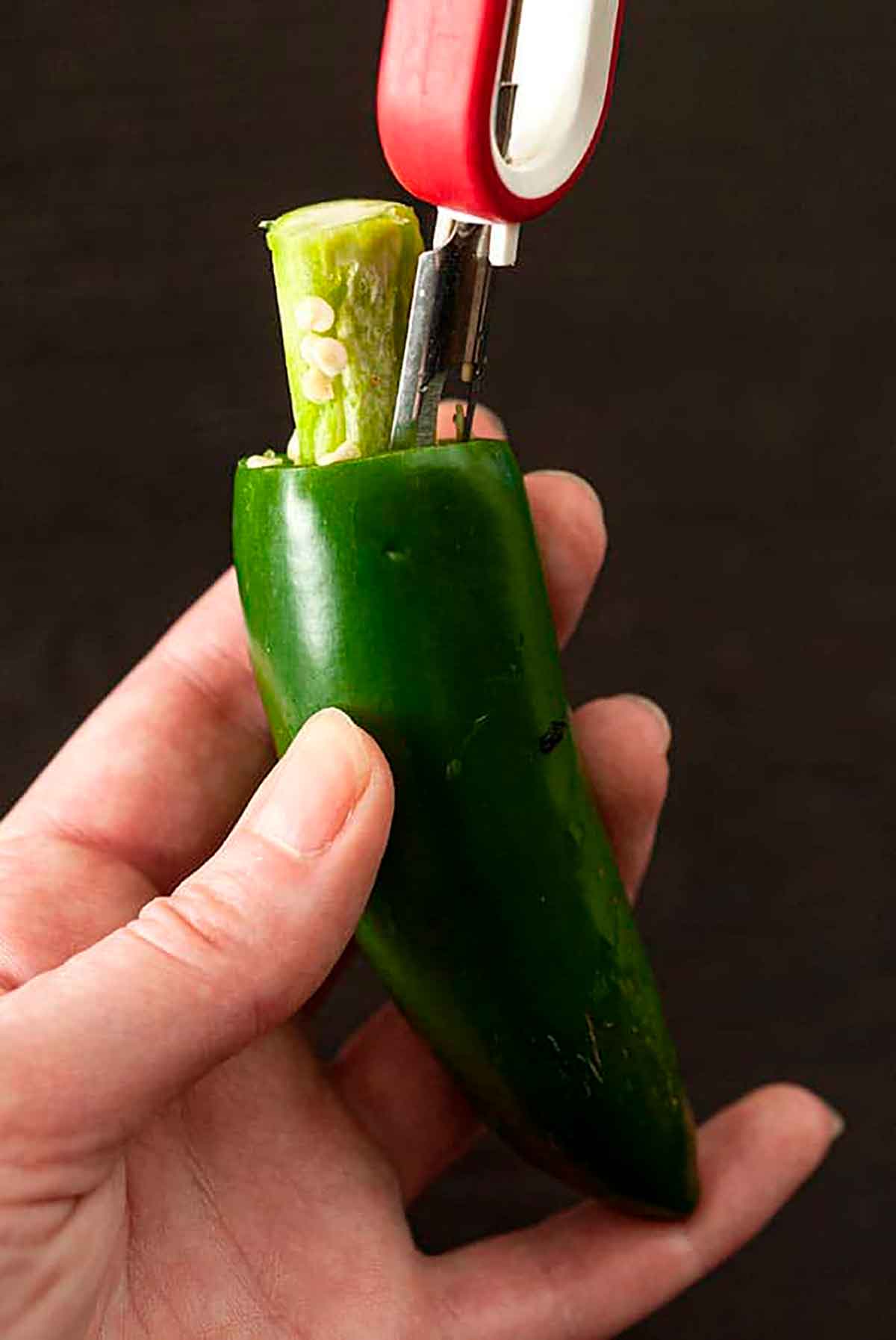 Hands using an apple peeler to remove the center of a jalapeño pepper.
