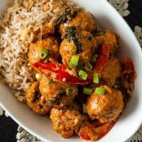 A bowl full of rice and coconut curry meatballs on a black table with a lace doily.