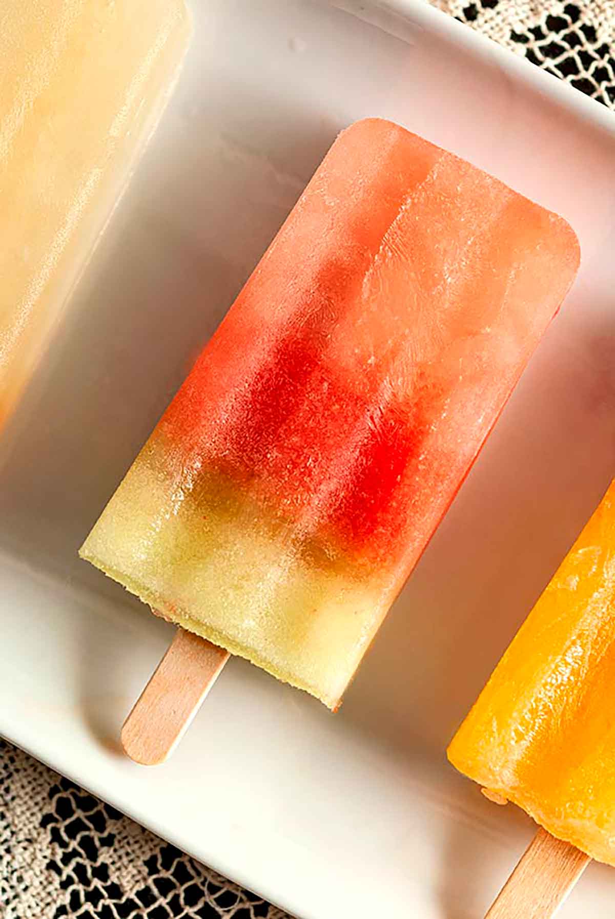A watermelon ice pop on a white plate between 2 other ice pops.