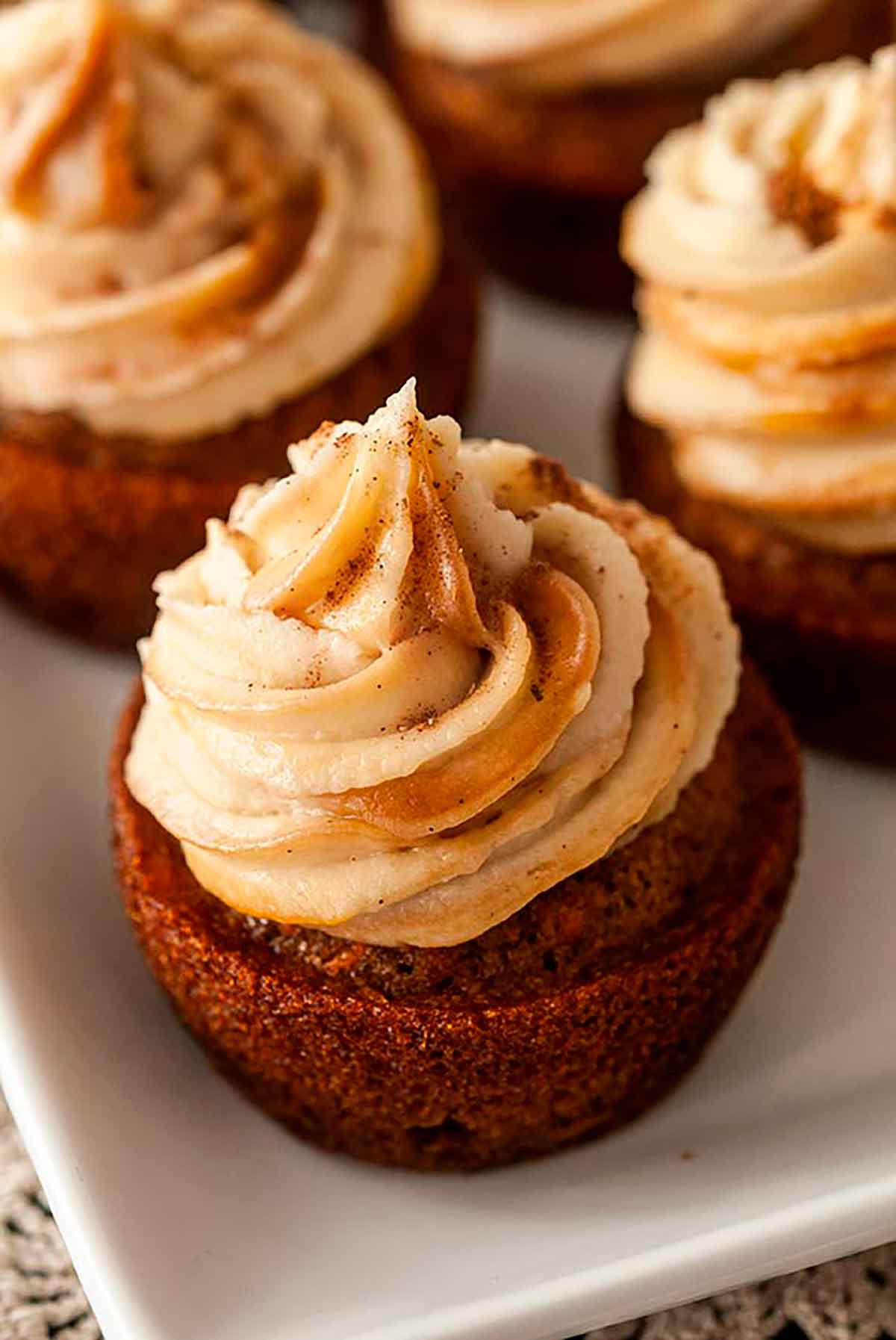 A frosted cupcake on a plate beside 3 others.