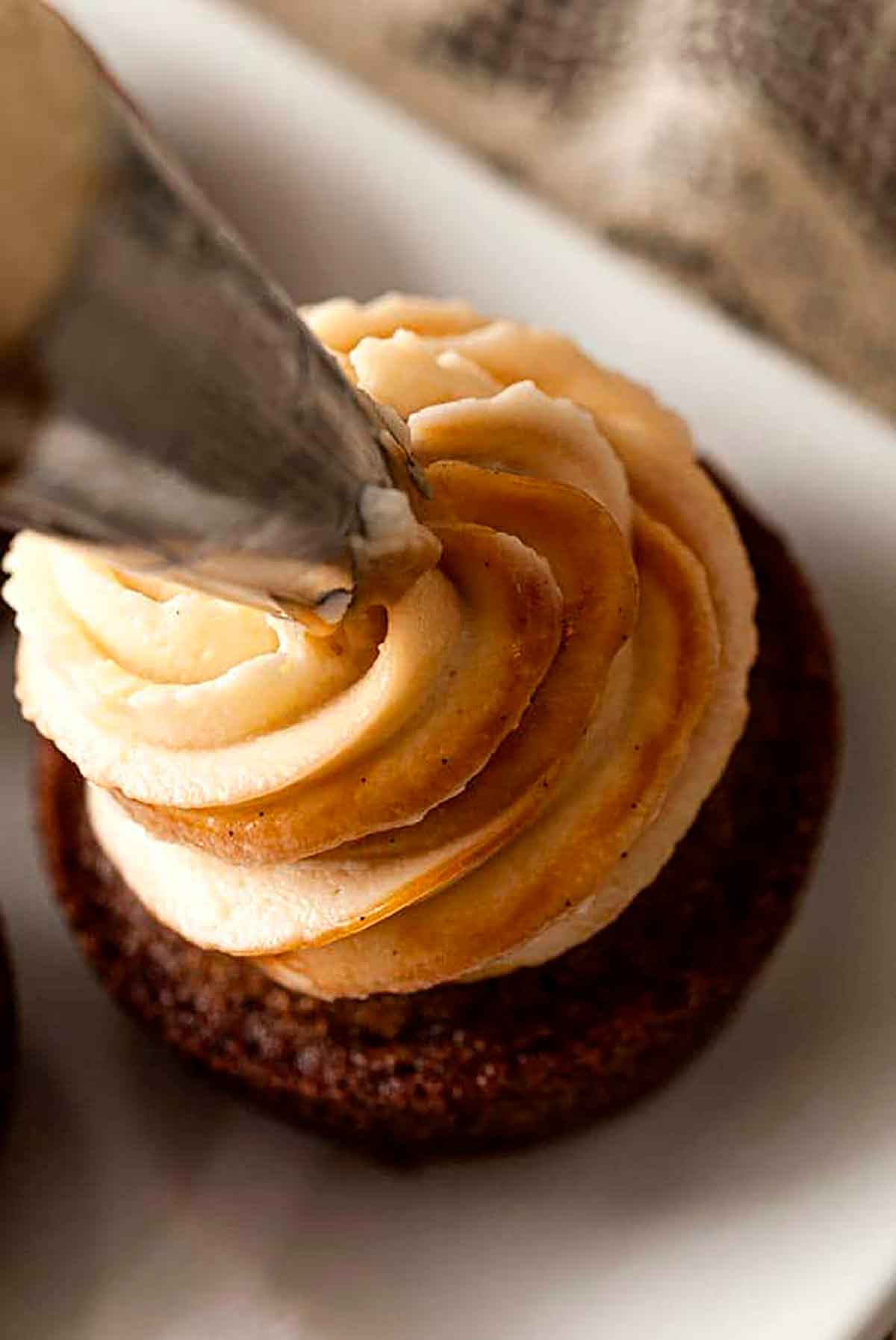 A cupcake being frosted with a pastry tip.