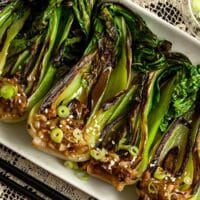 Seared baby bok choy on a plate, sitting on a table with a lace table cloth.