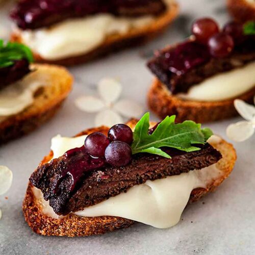 1 steak appetizer on a marble slate, garnished with tiny grapes, arugula and dripping cheese.