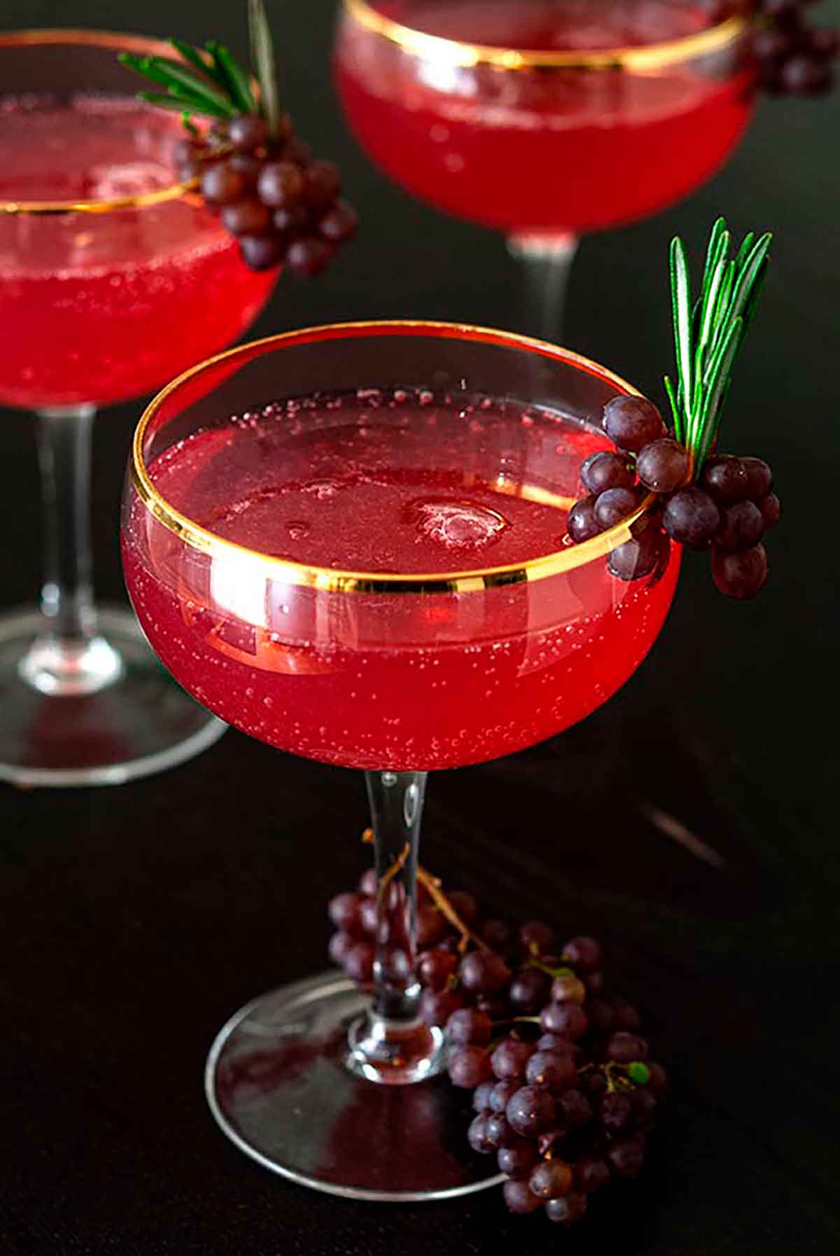 3 cocktails garnished with small grapes and sprigs of rosemary.