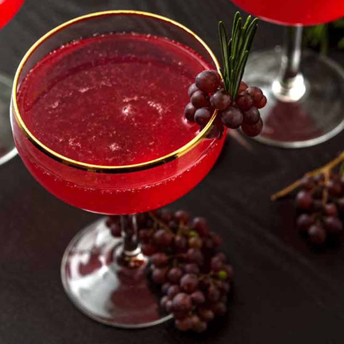 A cocktail garnished with small grapes and sprigs of rosemary.