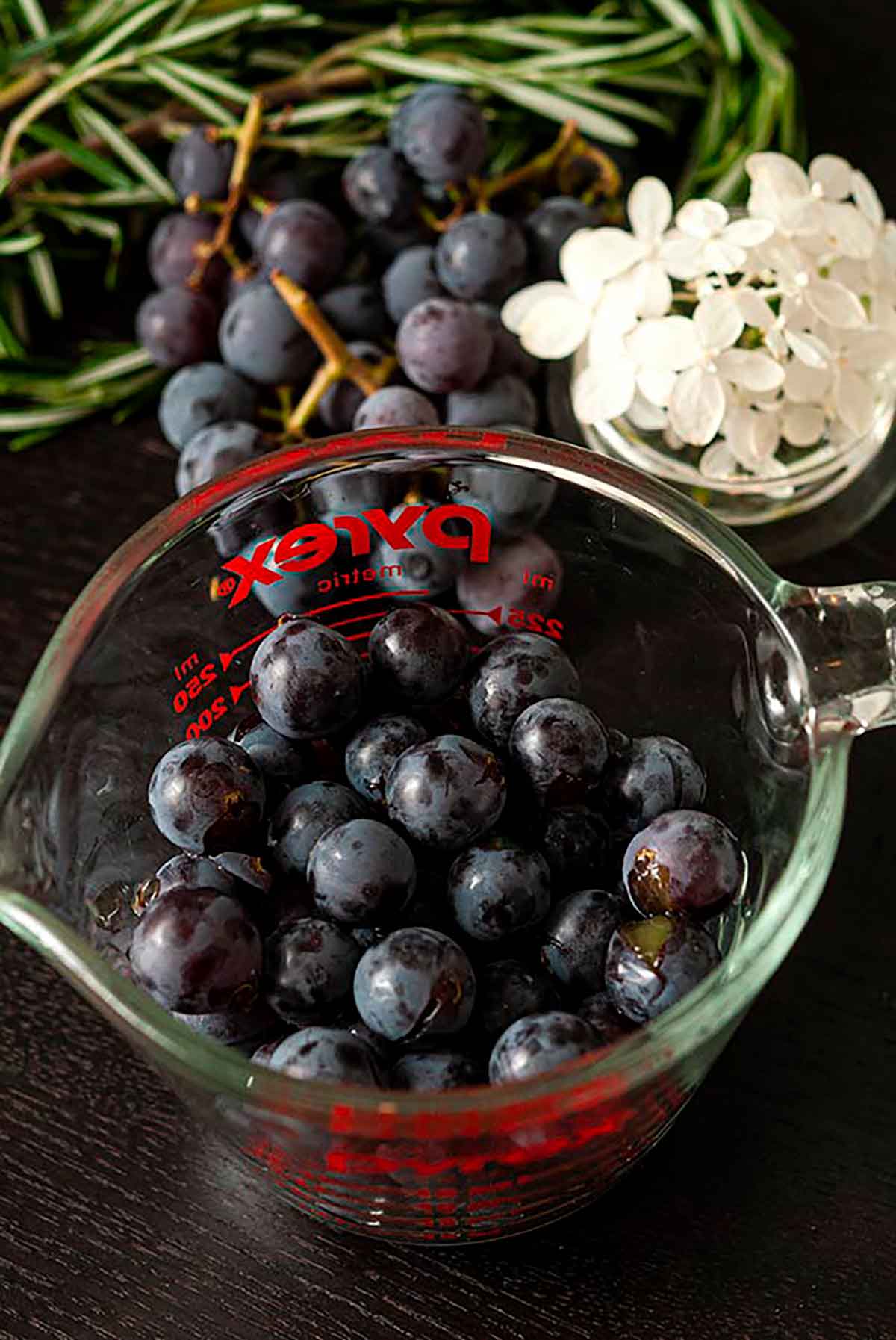 A measuring cup full of grapes beside a small bowl of flowers on a table.