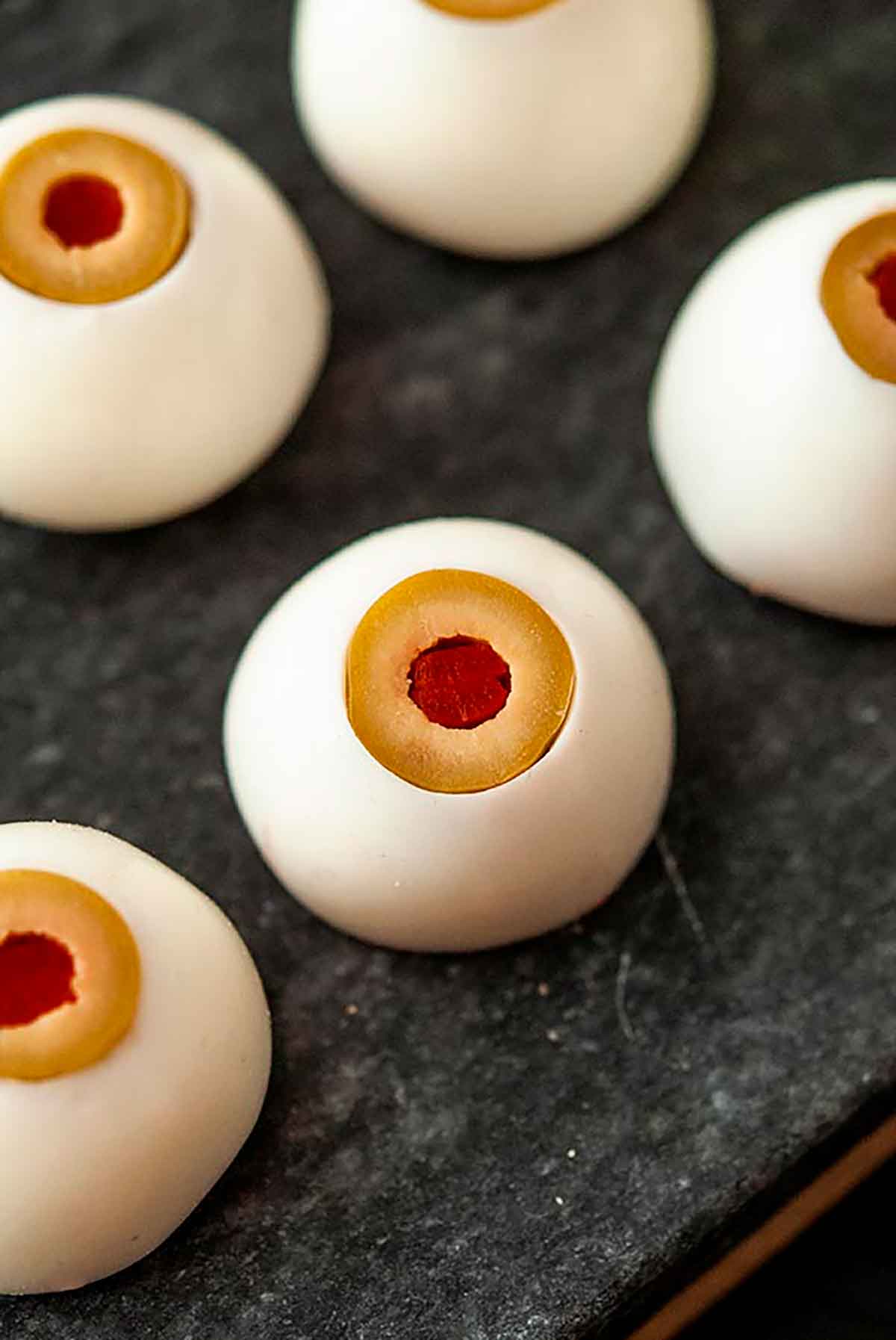 5 deviled eggs that look like eyeballs on a marble plate.