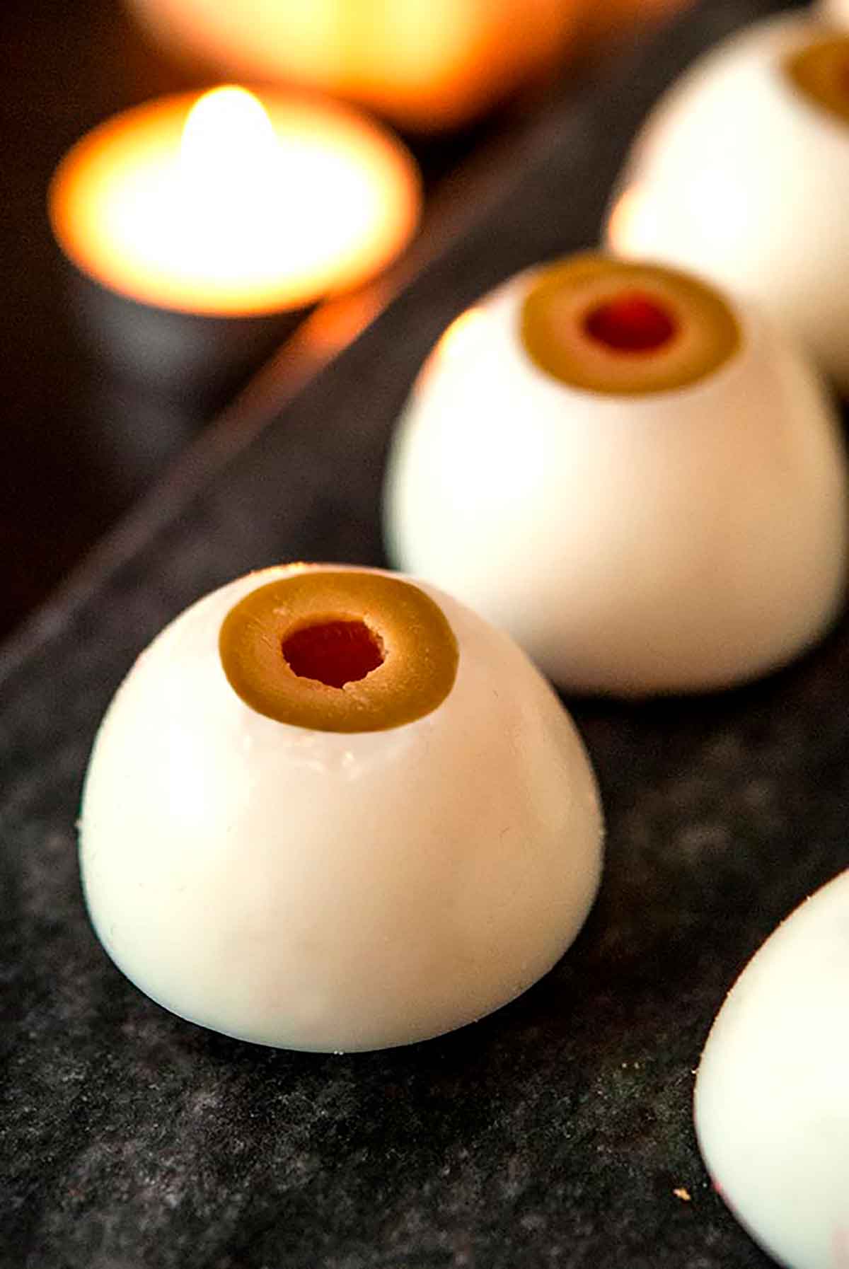 2 deviled eggs that look like eyeballs on a marble plate with a candle in the background.