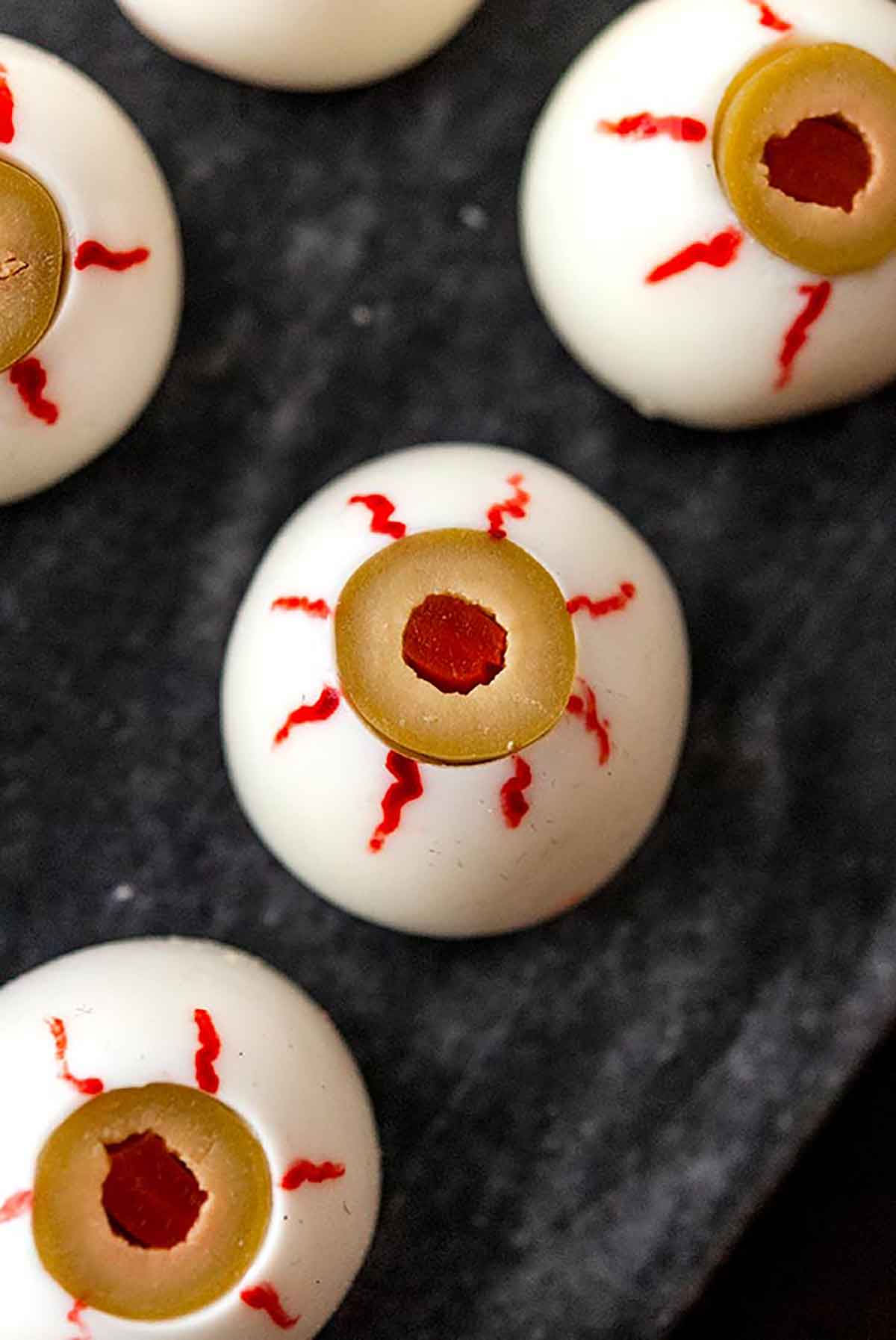 A deviled eyeball with little veins painted with dye on a marble plate surrounded by 3 others.