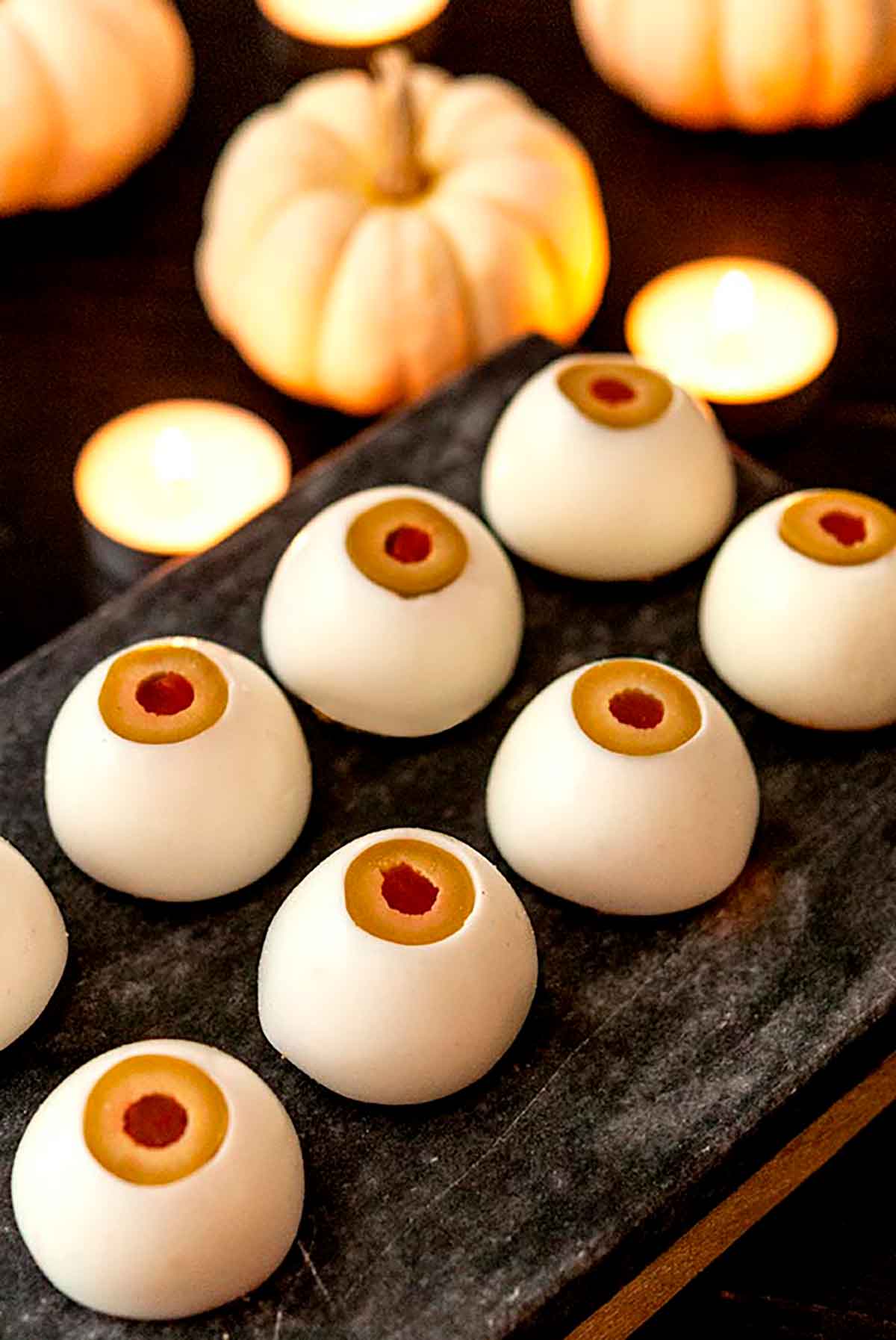 8 upside-down deviled eggs that look like eyeballs on a slate in front of candles and white pumpkins.