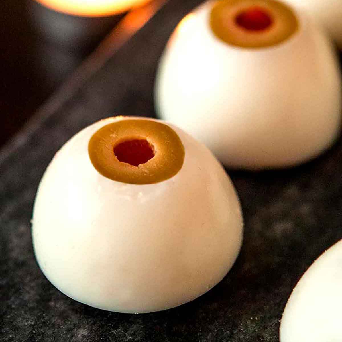 2 deviled eggs that look like eyeballs on a marble plate with a candle in the background.