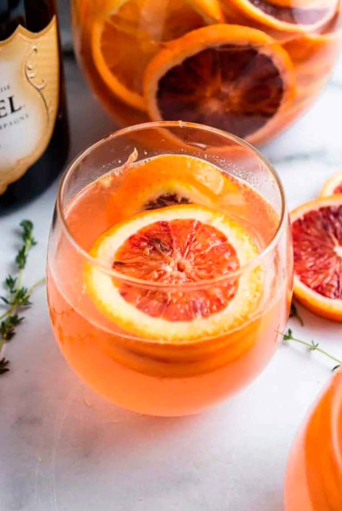 A blood orange champagne cocktail, garnished with an orange slice, beside a few stray orange slices on a table.
