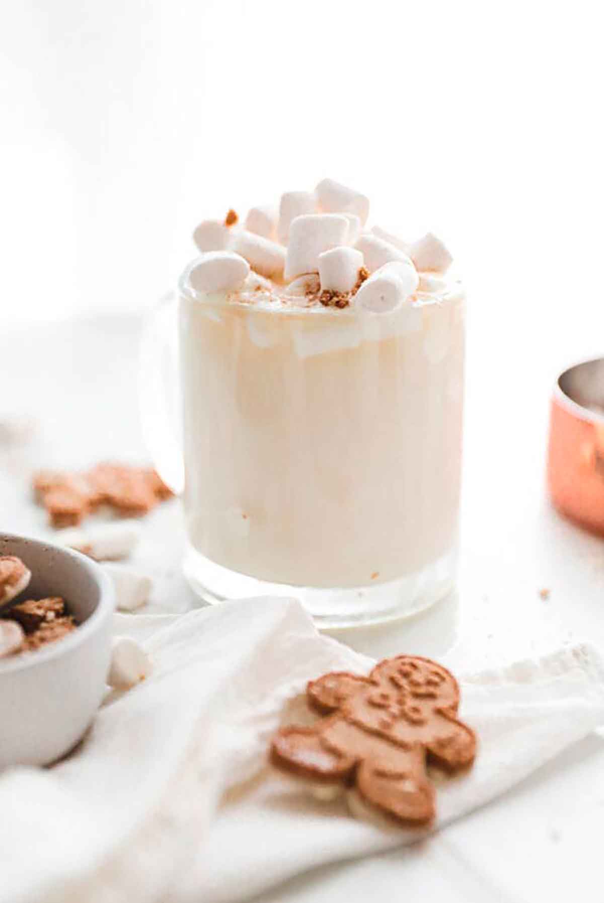 A creamy cocktail in a glass, topped with marshmallows and surrounded by cookies.