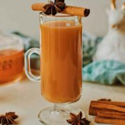 A cocktail in a mug, garnished with cinnamon, anise, and surrounded by cinnamon sticks and anise on a table.