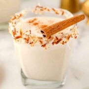 A coquito cocktail, garnished with toasted coconut and a cinnamon stick.