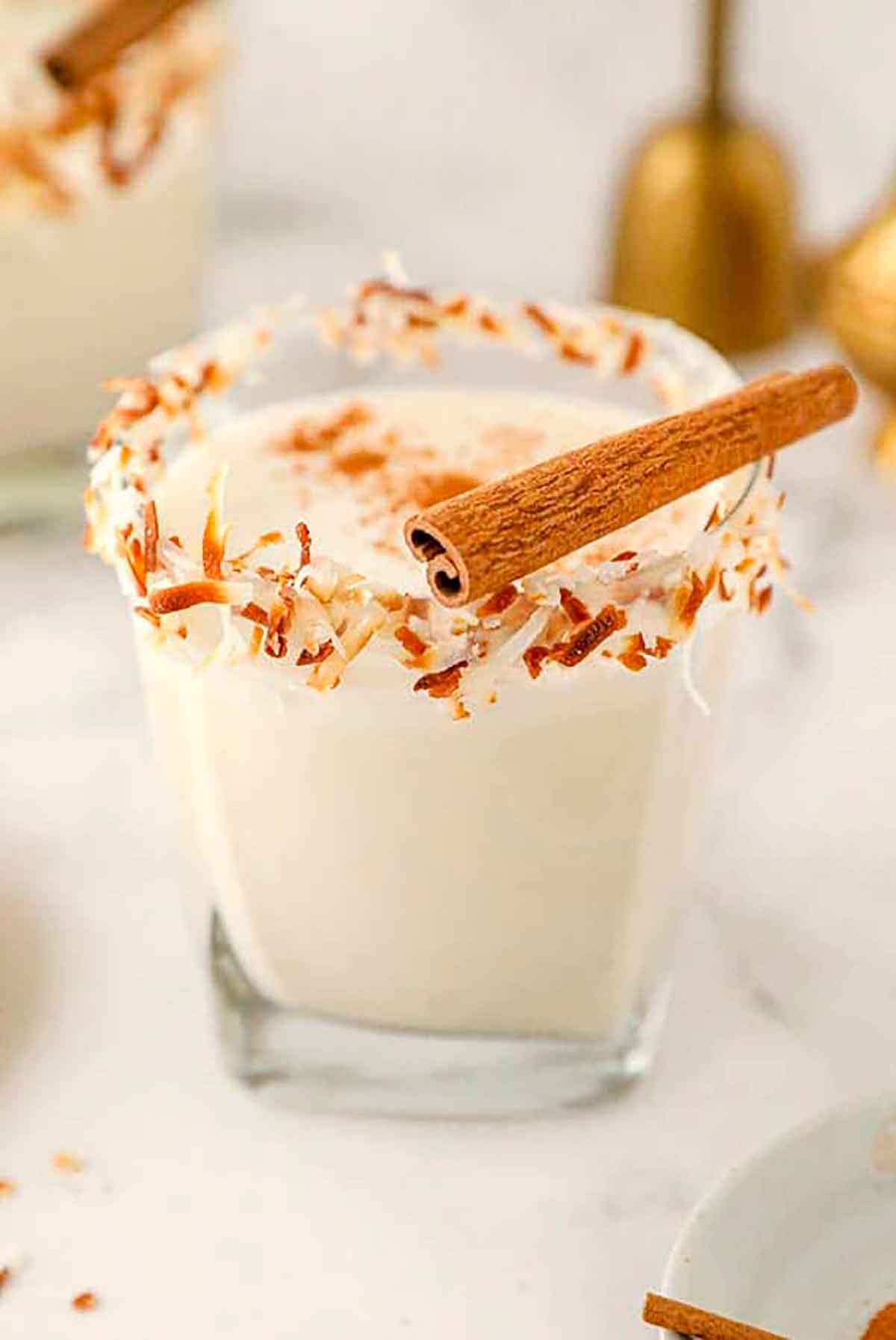 A coquito cocktail, garnished with toasted coconut and a cinnamon stick.