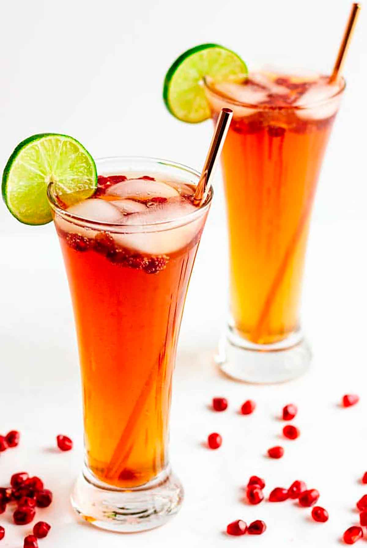 2 pomegranate lime spritzer cocktails, garnished with pomegranate seeds and lime slices.
