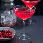 2 red cocktails in a dark setting, garnished with cranberries.