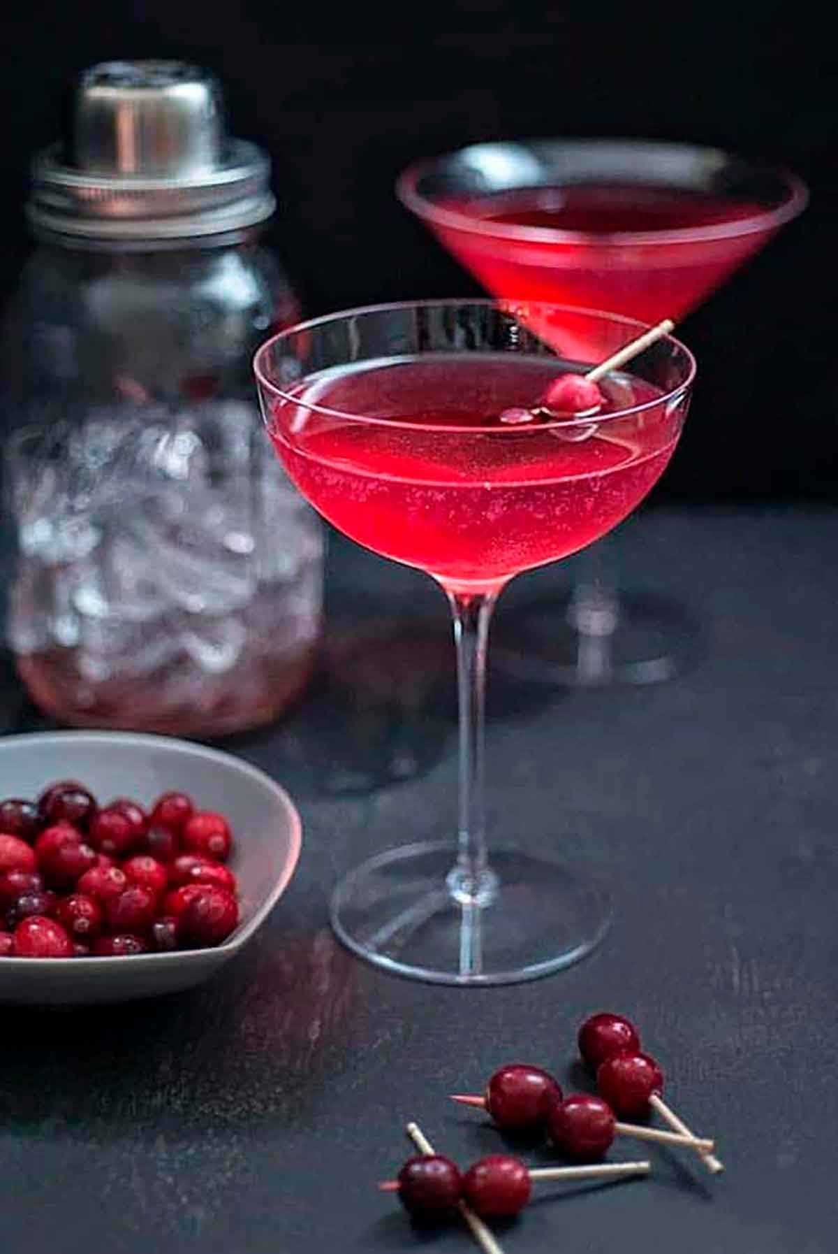 2 red cocktails in a dark setting, garnished with cranberries.