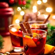 3 Gluhwein cocktails, garnished with cinnamon, orange and cranberries in a holiday setting.