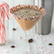 A creamy, chocolate cocktail beside a glass of candy canes and a cocktail shaker.