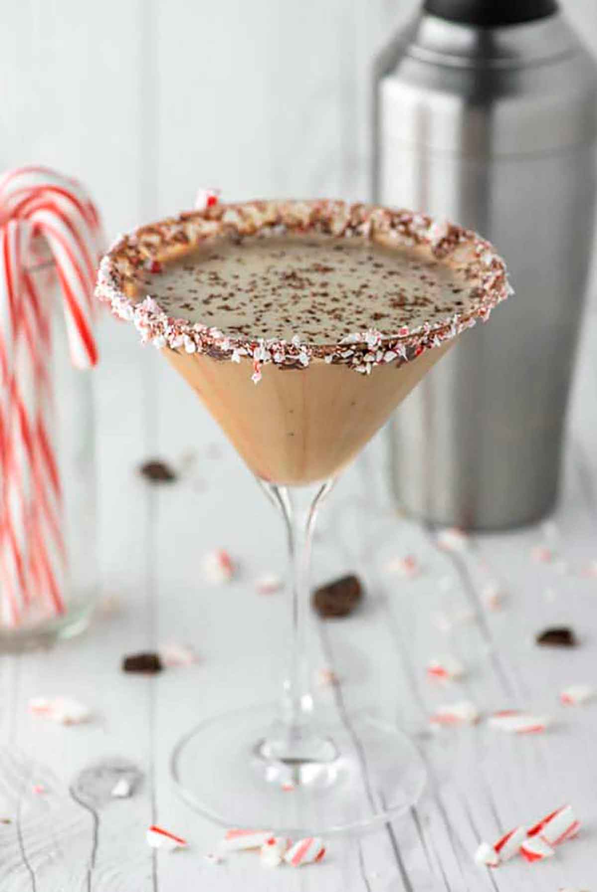 A creamy, chocolate cocktail beside a glass of candy canes and a cocktail shaker.