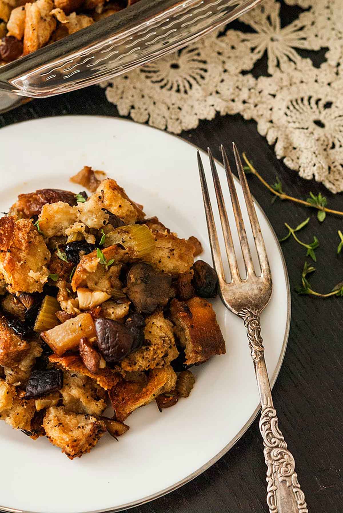 A plate of stuffing with a victorian-style fork on a black table with a lave table cloth and a few sprinkles of thyme.