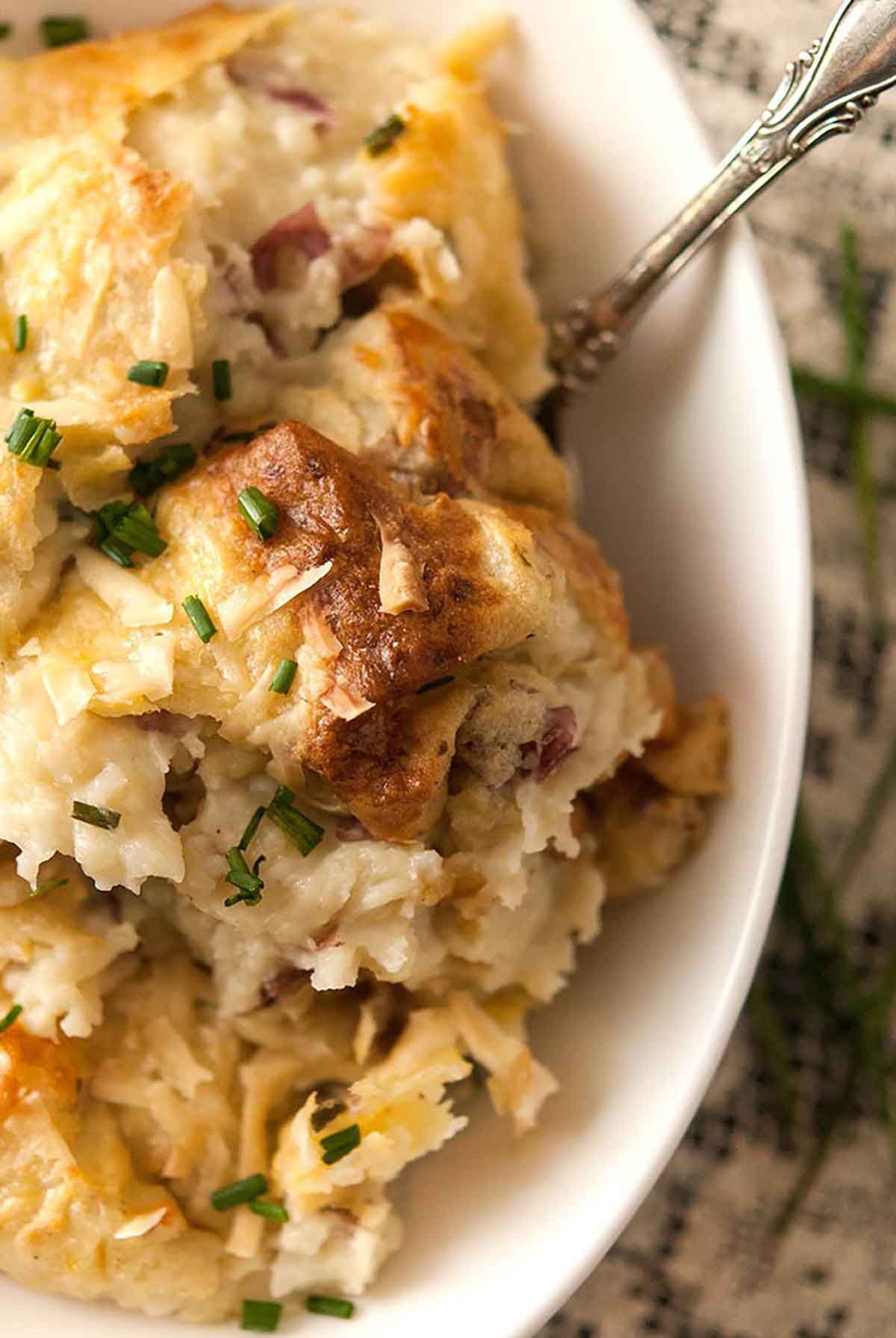 A bowl of baked mashed potatoes on a table with a lace tablecloth.