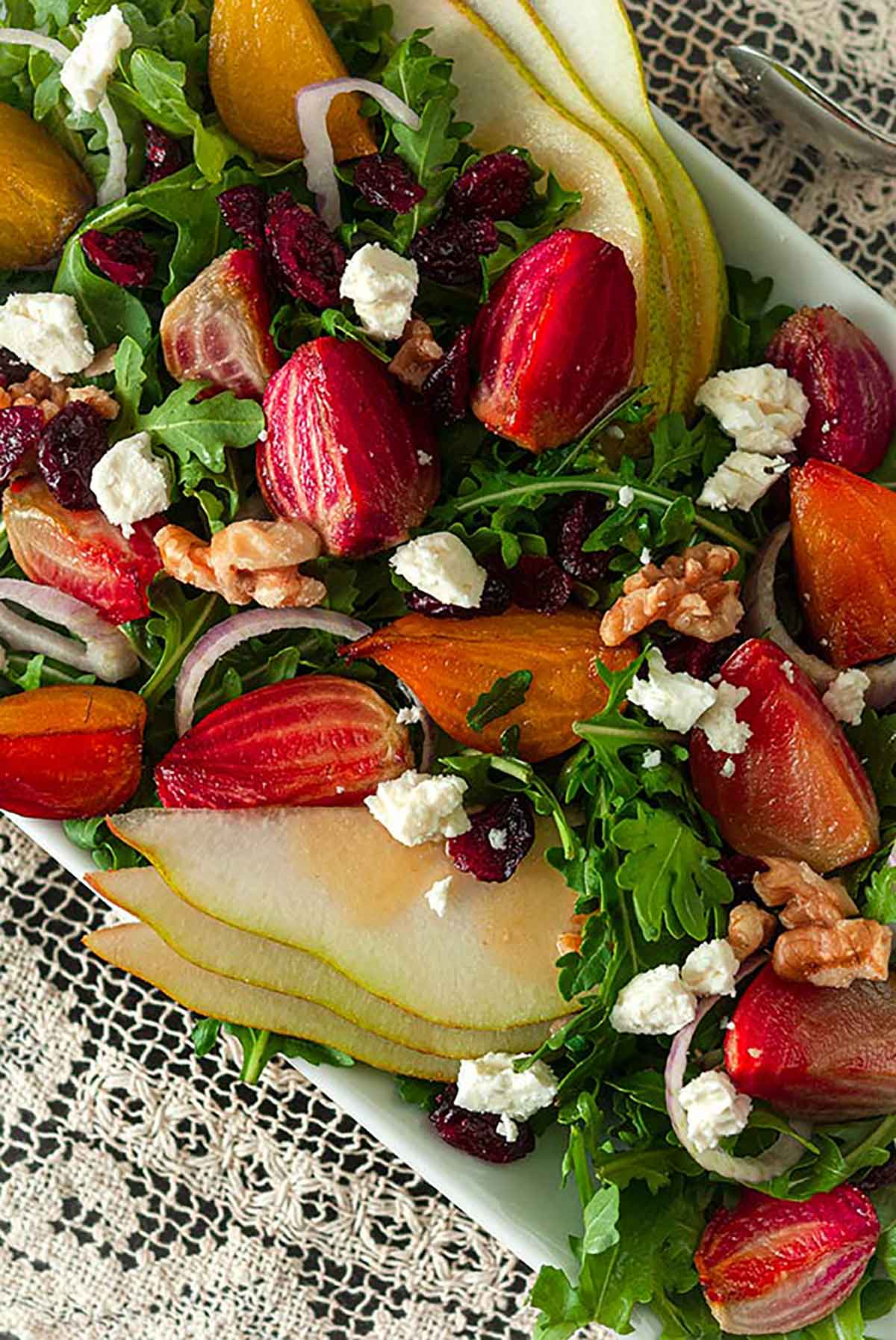 A salad with colorful vegetables, pears, berries and nuts on a lace table cloth.