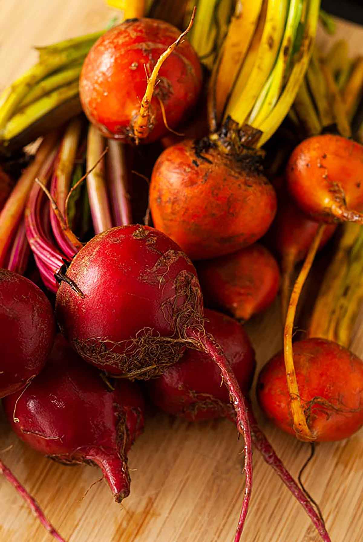 2 varieties of raw beets on a wooden cutting board.