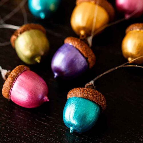 12 painted acorn ornaments on a table, in different colors.