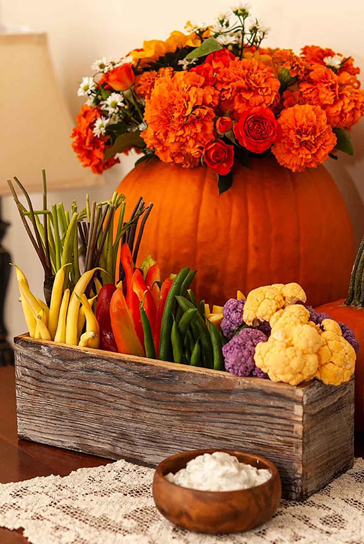 A flower box crudités on a table in front of a pumpkin full of flowers.