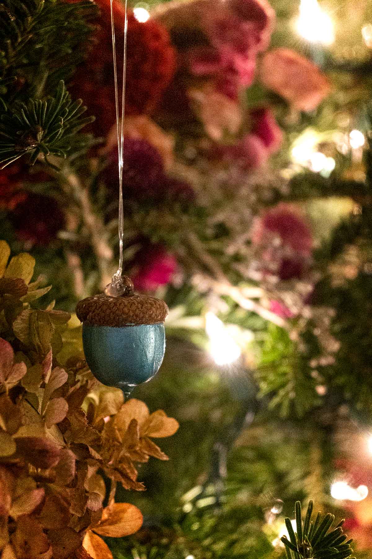 A blue metalic-painted acorn hanging in a decorated Christmas tree.