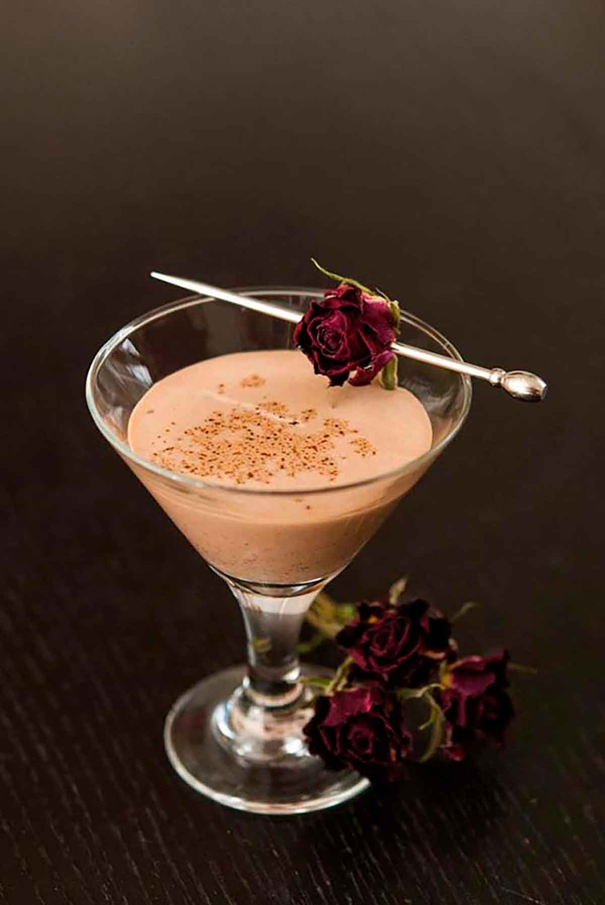 A small glass of Mexican chocolate liqueur sprinkled with cinnamon on a black table with small roses for garnish.
