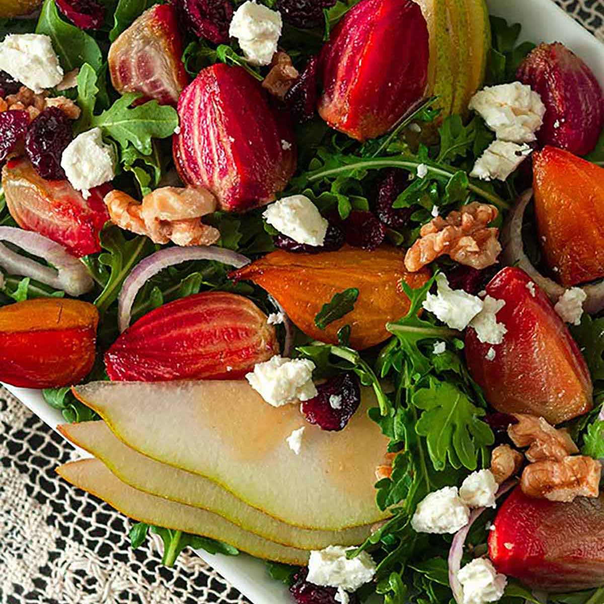 A salad with colorful vegetables, pears, berries and nuts on a lace table cloth with plates and forks in the background.