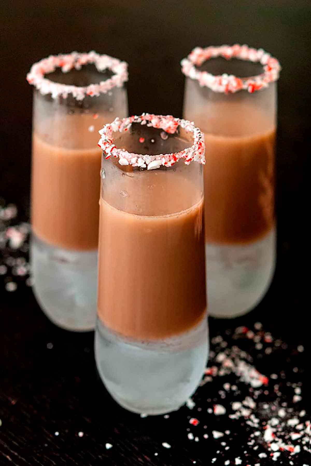 3 chocolate cocktails, rimed with crushed candy cane on a black table.