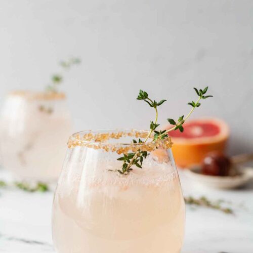 2 cocktails garnished with thyme on a marble table.