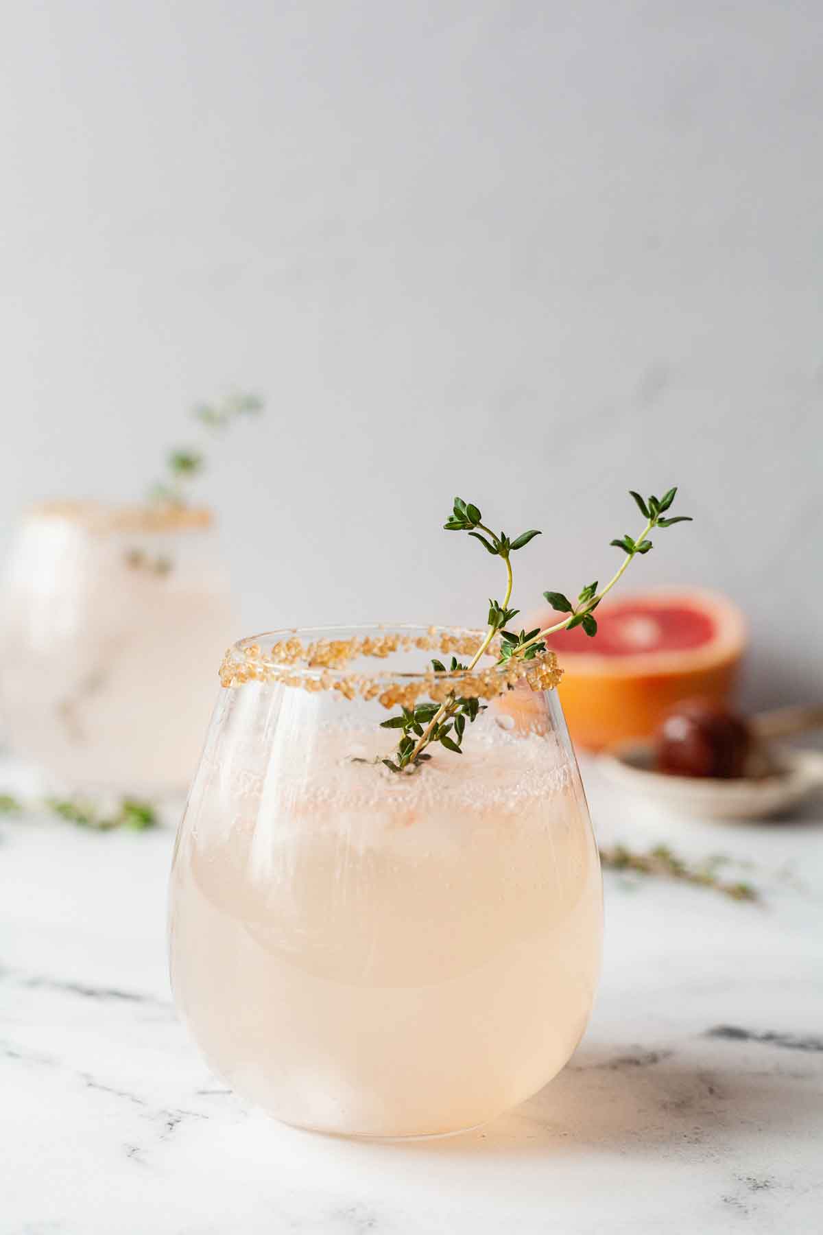 2 cocktails garnished with thyme on a marble table.