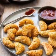 A metal tray of small pasties beside a spoon with sauce.