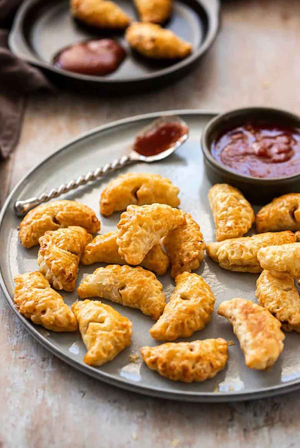 A metal tray of small pasties beside a spoon with sauce.