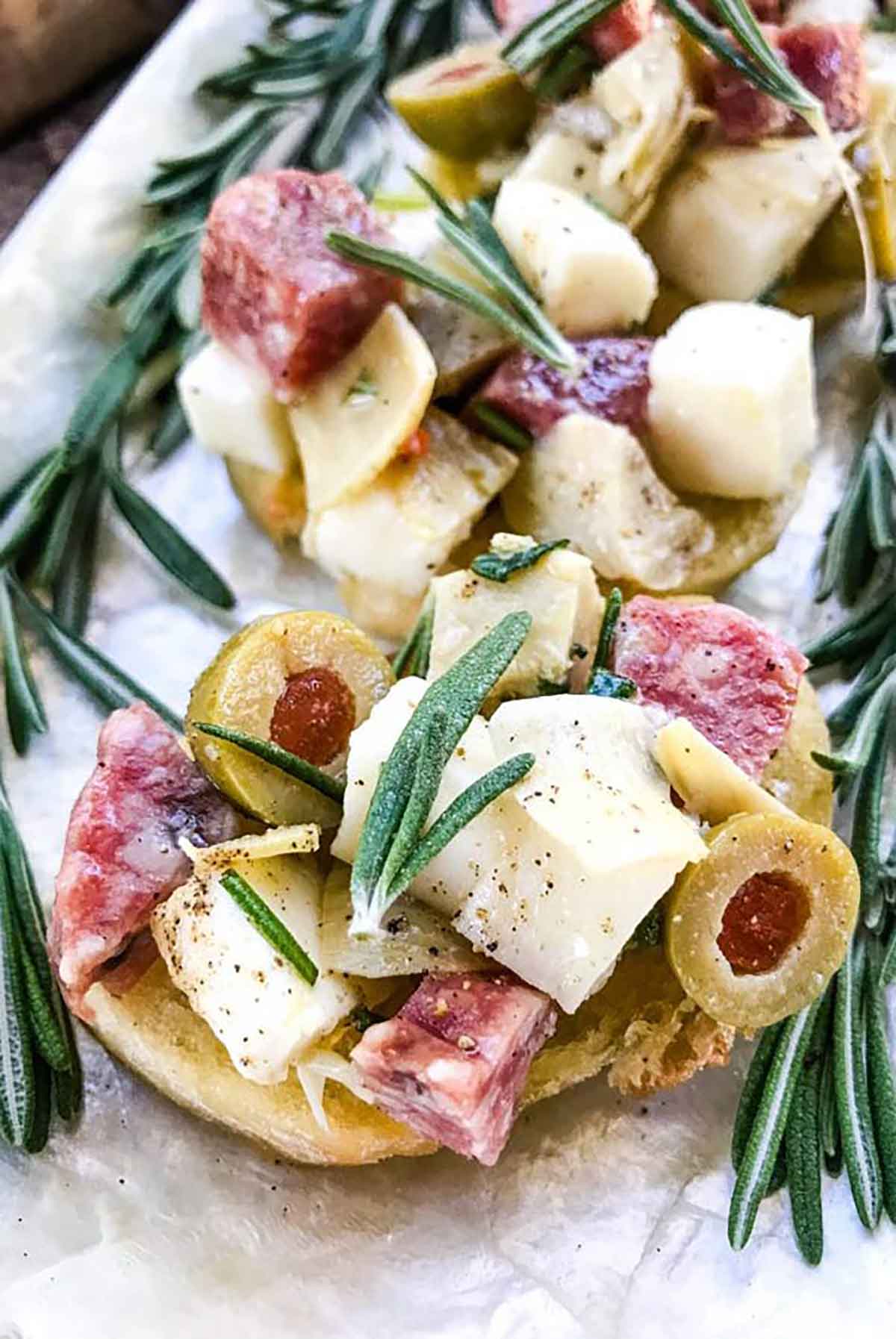 3 antipasti appetizers with cheese, olives, meat and rosemary on a plate.