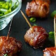 6 bacon-wrapped chestnuts on a slate beside a scallion sauce.