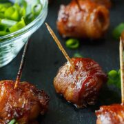 6 bacon-wrapped chestnuts on a slate beside a scallion sauce.