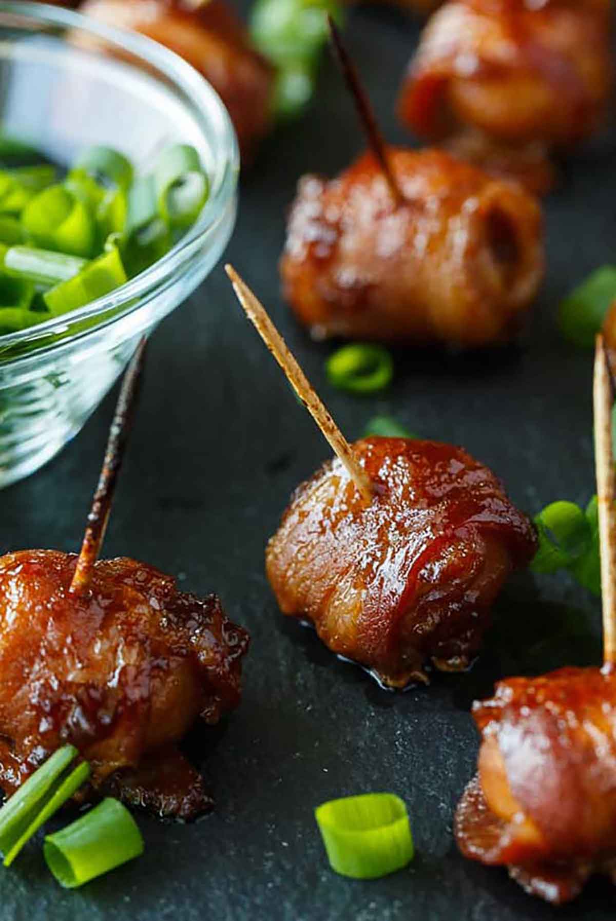 6 bacon-wrapped chestnuts on a slate beside a scallion sauce.
