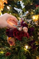 A hand placing a flower bouquet on a Christmas tree.