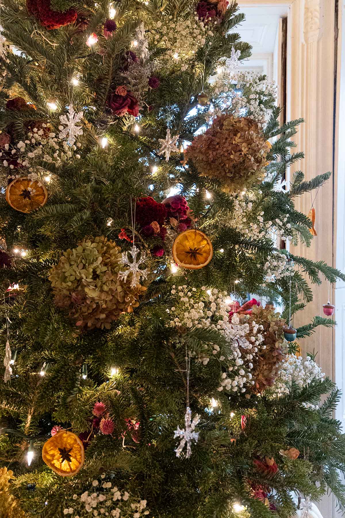 A Christmas tree with baby's breath and flower decorations, dry oranges and glass snowflakes..