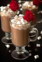 3 Hot chocolates, topped with marshmallows and flower garnishes on a table, sprinkled with marshmallows and chocolate chips.