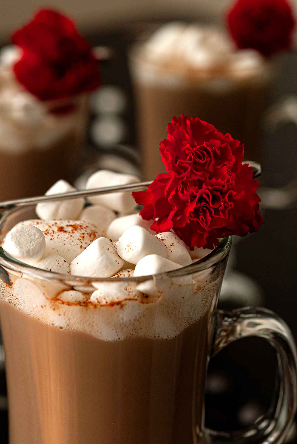 3 hot chocolates topped with marshmallows and garnished with flowers.
