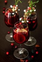 3 glasses of sangria garnished with fruits, flowers, herbs and star anise, with a few scattered cranberries and blackberries.